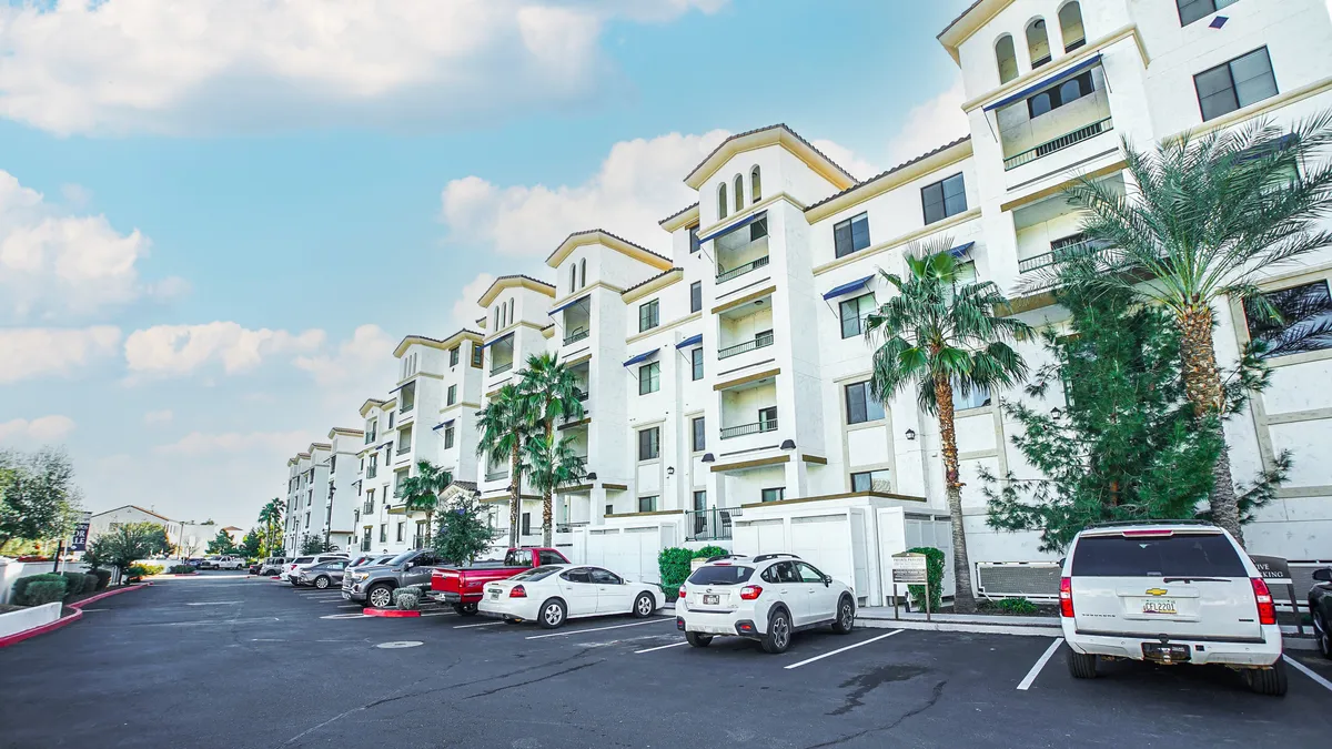 The apartment building’s facade is framed by tall palm trees, with a sun-filled parking area where cars are parked. The exterior shot reflects a welcoming, communal atmosphere, and hints at the property’s accessibility and connection to the broader Chandler area.
