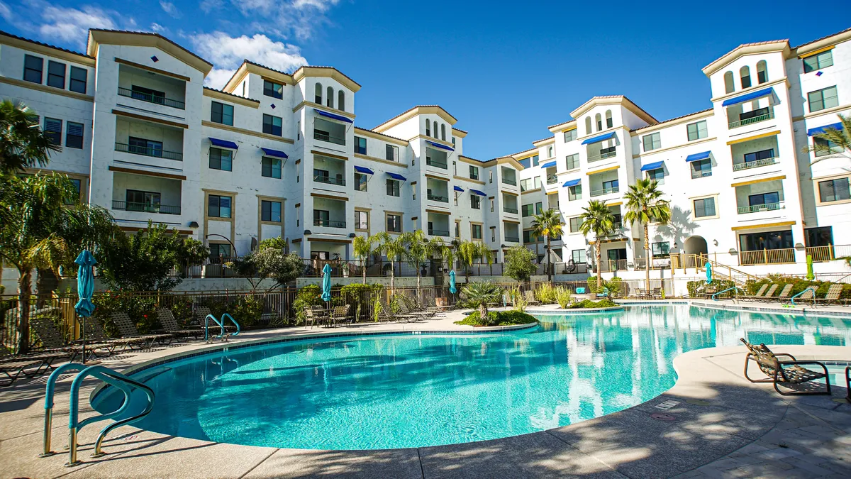 A resort-style swimming pool surrounded by palm trees and lounge chairs, set against the backdrop of the residential building. The setting is tranquil and exclusive, offering opportunities for relaxation and socializing within the secure complex.