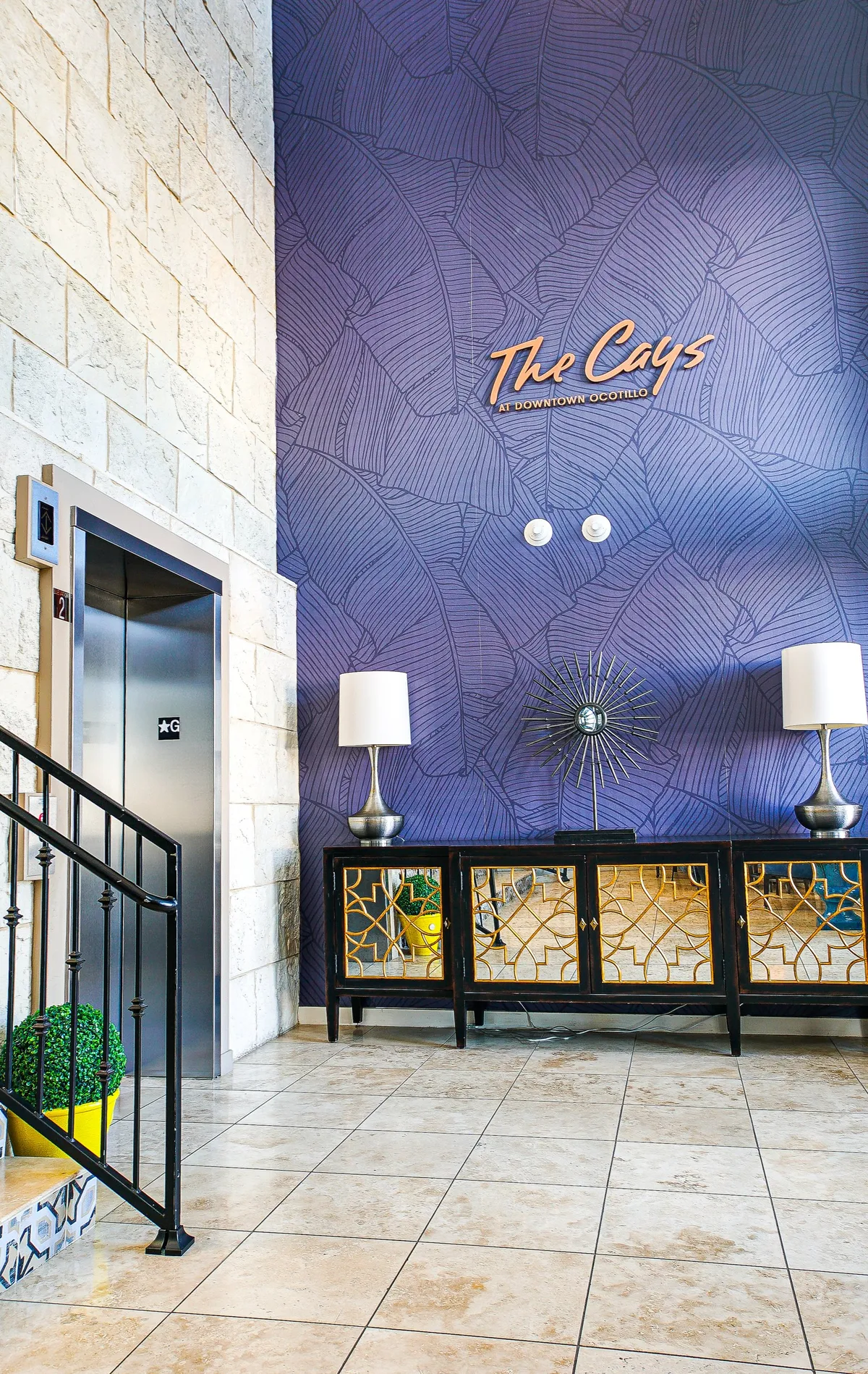 A stylish lobby area featuring an elevator, a decorative console table adorned with lamps, and elegant wall art. The space is inviting and sets the tone for arrival and departure, hinting at both security and accessibility.