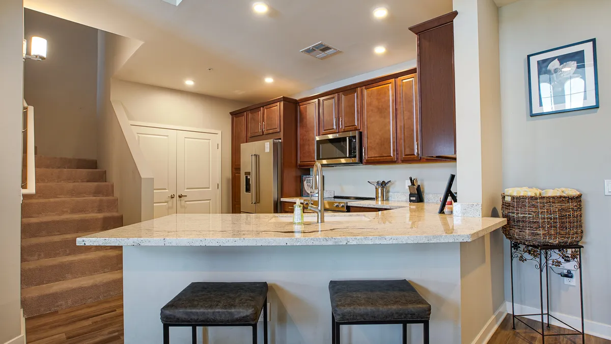 This image captures the gourmet kitchen, featuring a spacious island with stools, sleek stainless steel appliances, warm wooden cabinets, and plenty of counter space. Sunlight filters in, highlighting the breakfast bar and inviting ambiance ideal for both casual mornings and festive gatherings.