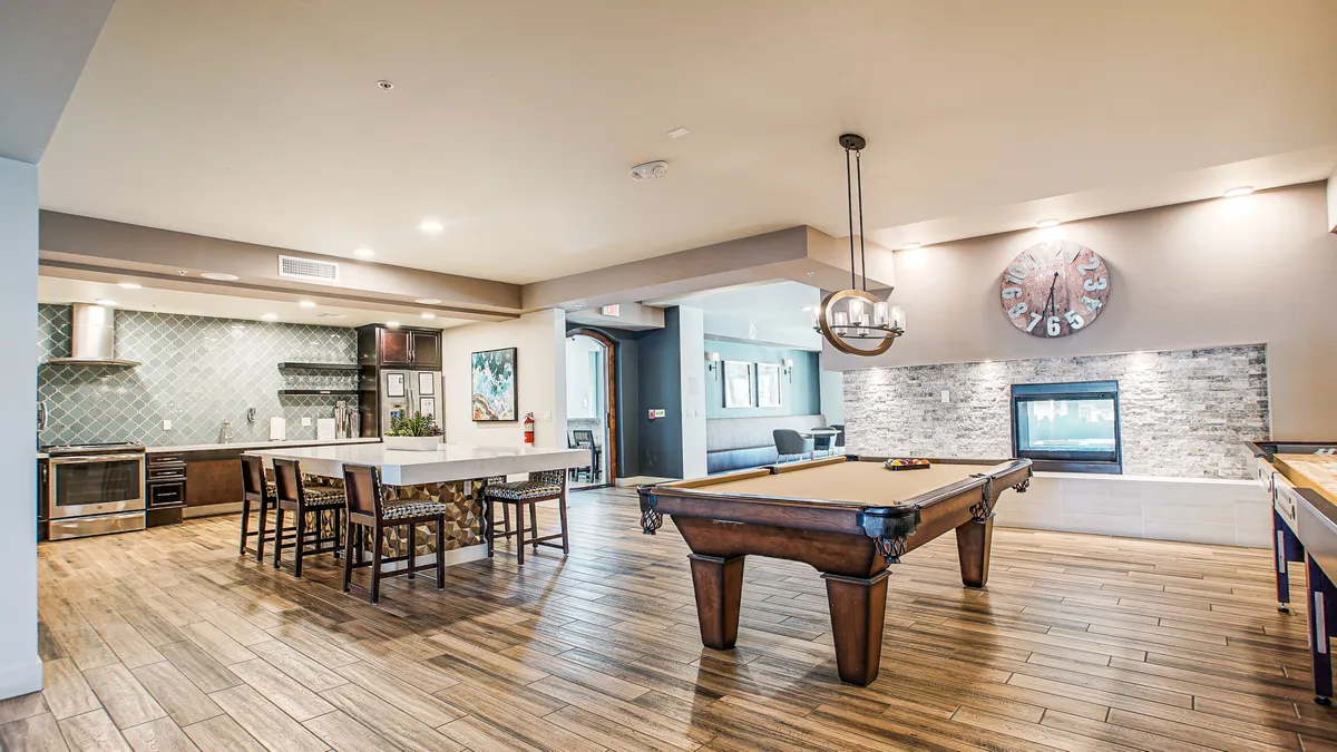 A stylish clubhouse interior featuring a pool table, fireplace, kitchen area, and cozy seating. The space is designed for social gatherings, relaxation, and entertainment, creating a welcoming community hub.