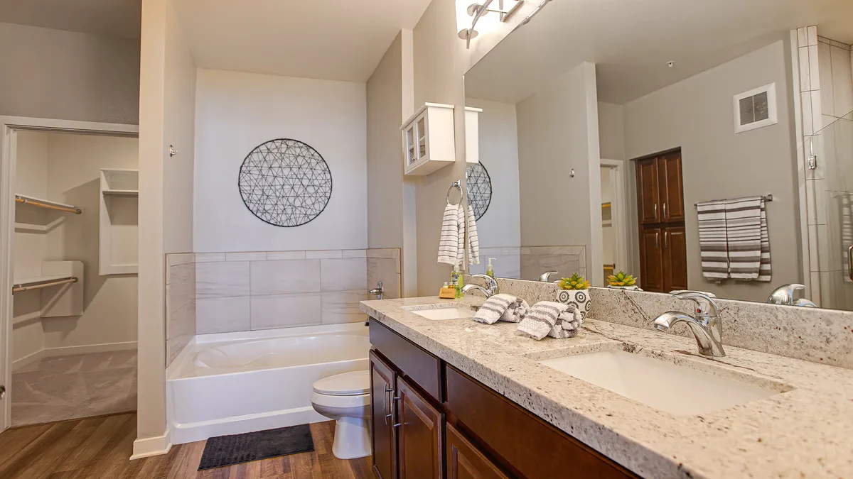 A luxurious bathroom featuring a dual sink vanity, a deep soaking bathtub, a large wall mirror, and decorative wall art. The bathing area is designed for comfort and indulgence, inviting guests to unwind and rejuvenate.