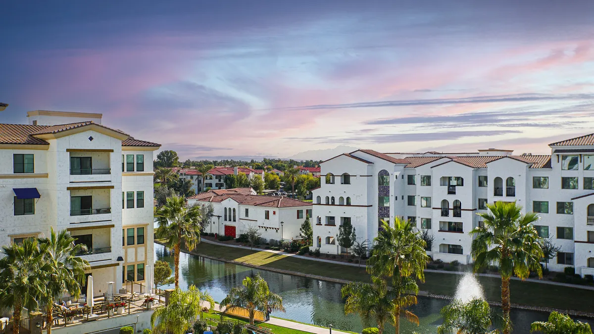 A serene canal lined with palm trees and flanked by contemporary buildings, with balconies overlooking the water. The peaceful setting suggests opportunities for strolls, outdoor relaxation, and community activities by the waterfront.