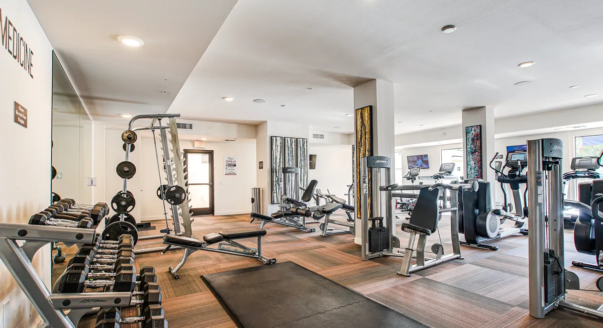 A bright, modern fitness center with weightlifting equipment, cardio machines, and a mirror wall. The space is well-lit and designed for a variety of workouts, inviting residents to prioritize wellness and active living.